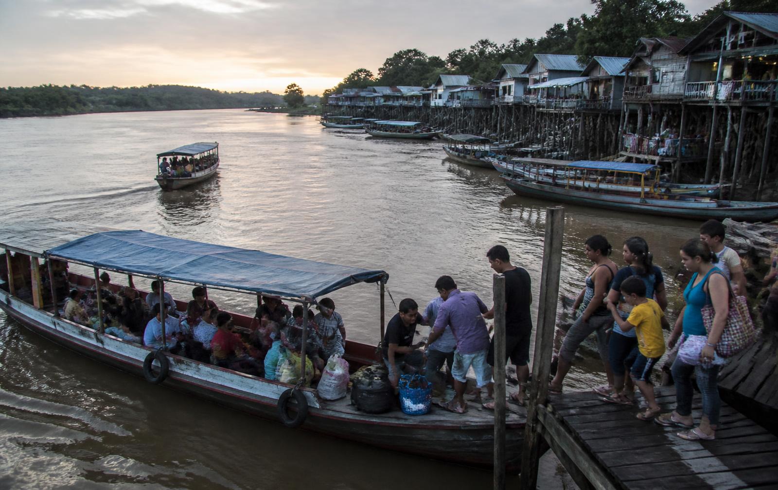Barcos de passageiros atracados em uma vila ribeirinha ao entardecer, com pessoas embarcando